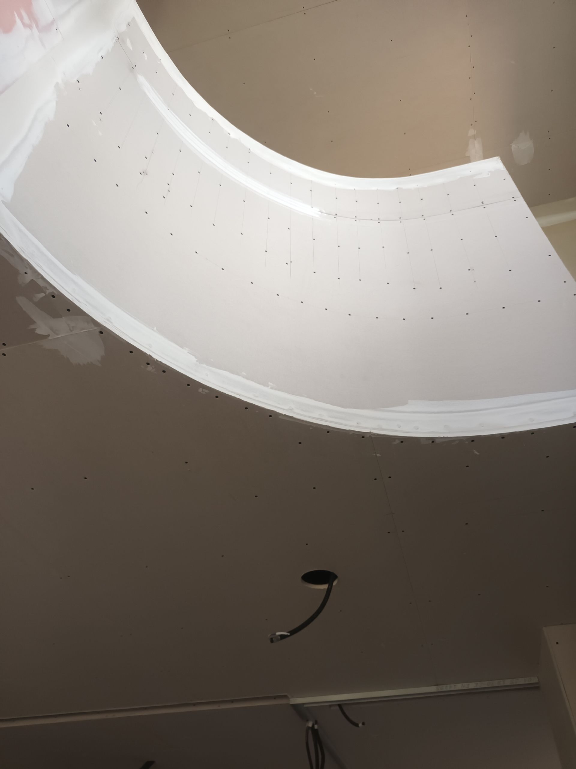 Plafond incurvé blanc avec soffite, ouverture encastrée et fil électrique suspendu dans une pièce beige