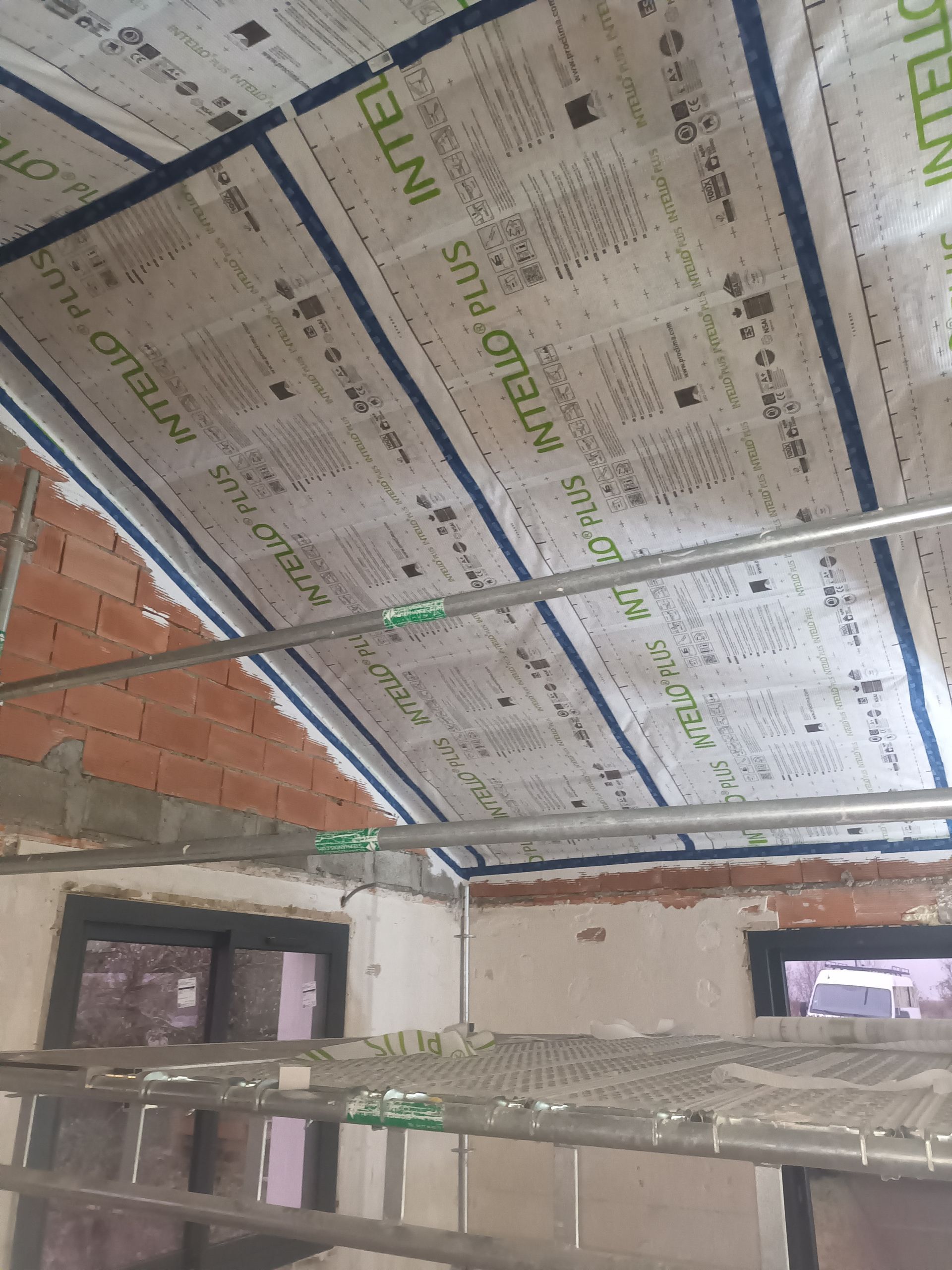 Intérieur en cours de construction avec panneaux de plafond isolés, charpente métallique et échafaudages en dessous.