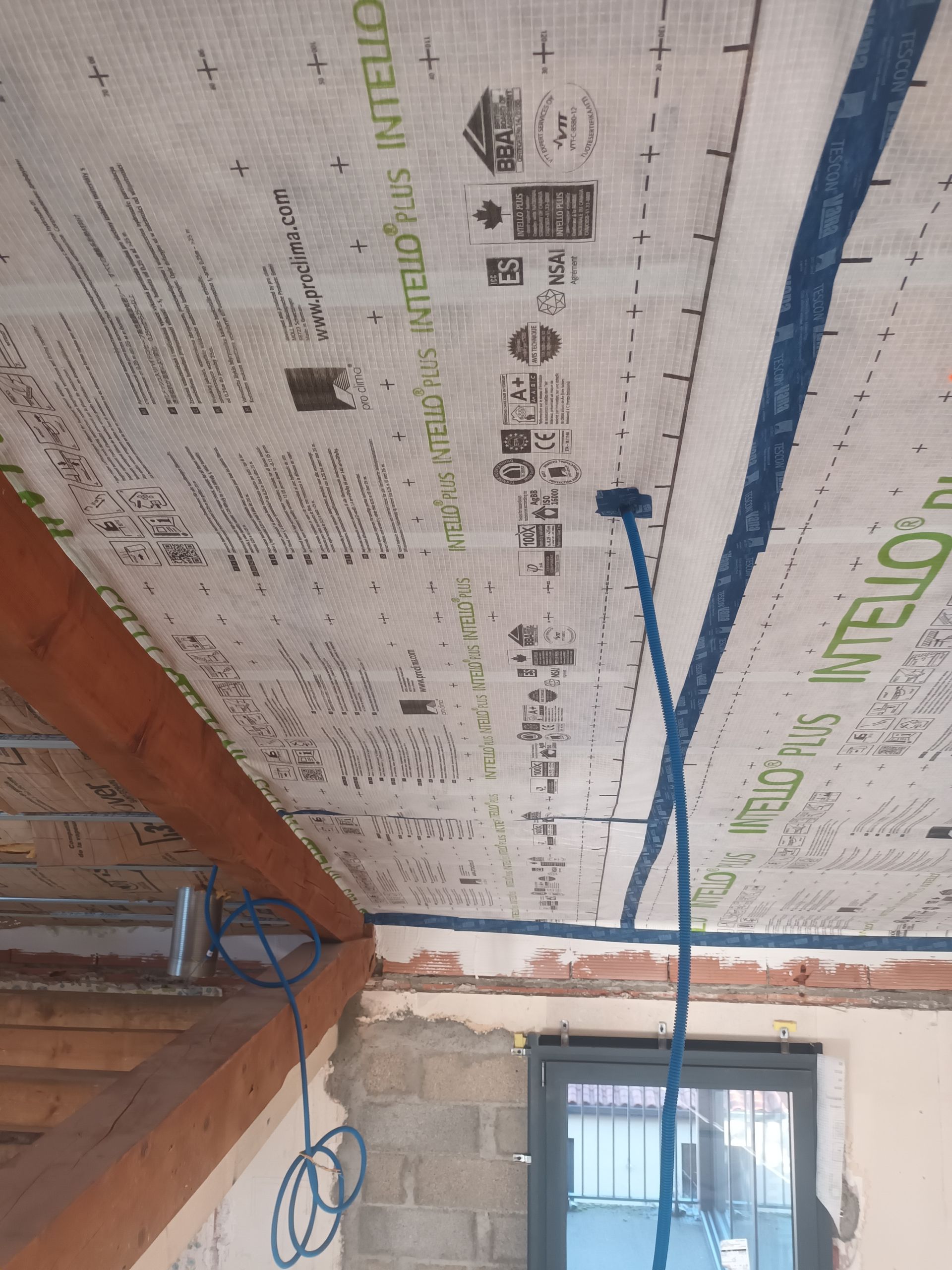 Plafond partiellement fini avec panneaux isolants, ruban adhésif bleu, câblage apparent et une porte en dessous