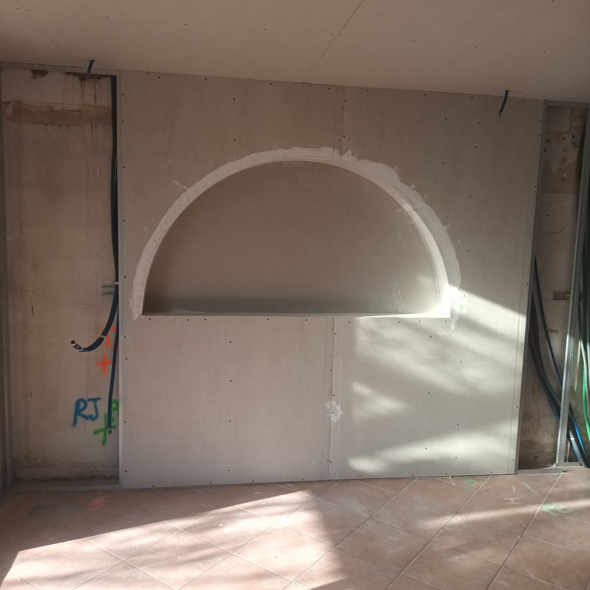 Mur intérieur inachevé avec une grande niche semi-circulaire et des câbles apparents sur les côtés.