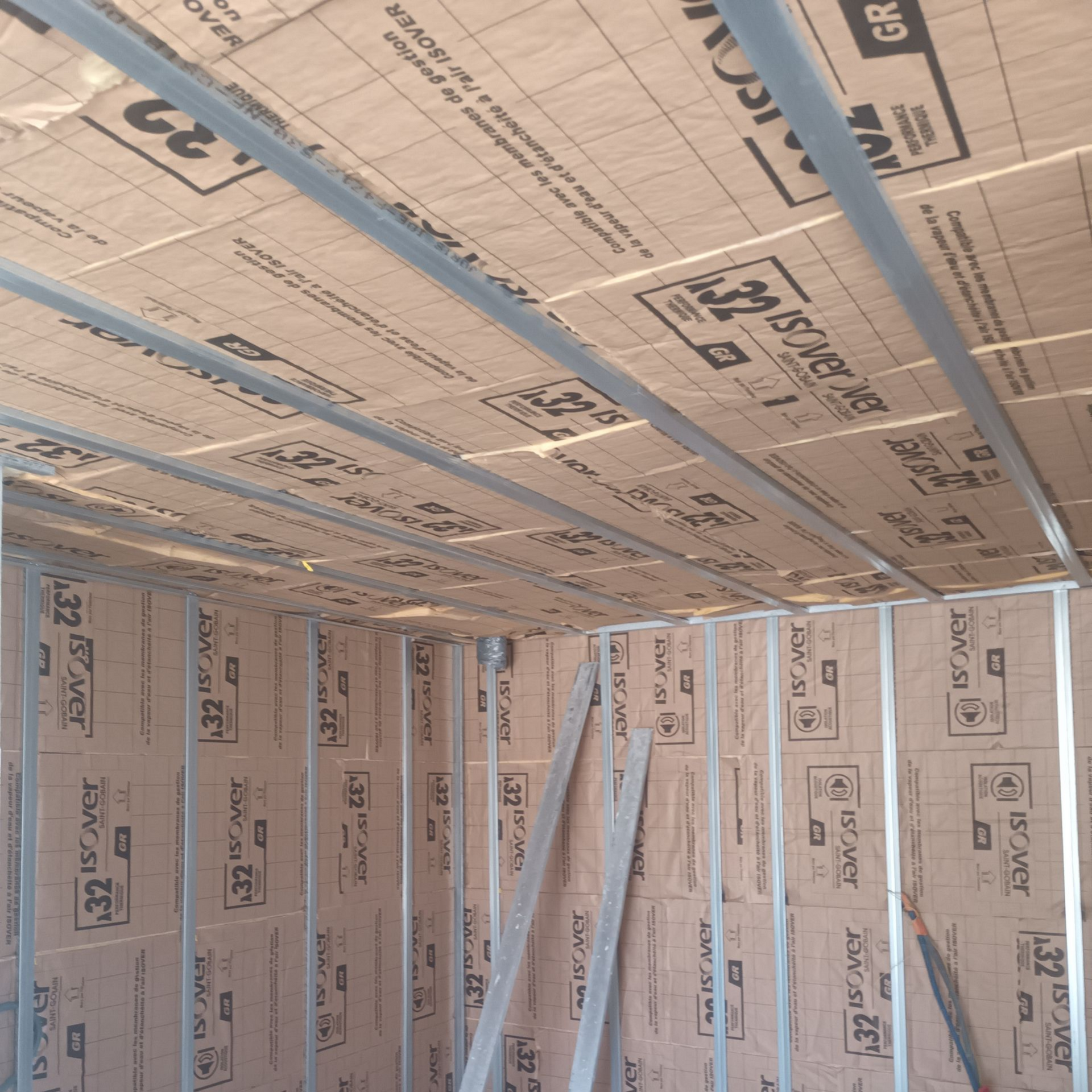 Pièce isolée en construction, avec une ossature bleue et des panneaux de mousse rose recouvrant les murs et le plafond.