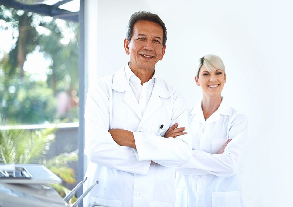 Dos médicos con batas blancas de pie con los brazos cruzados en una clínica luminosa.