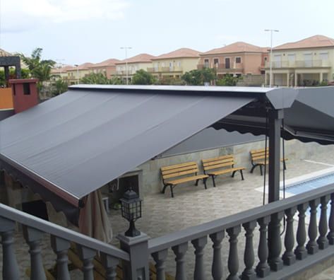 Un balcón con toldo negro sobre un patio con bancos.