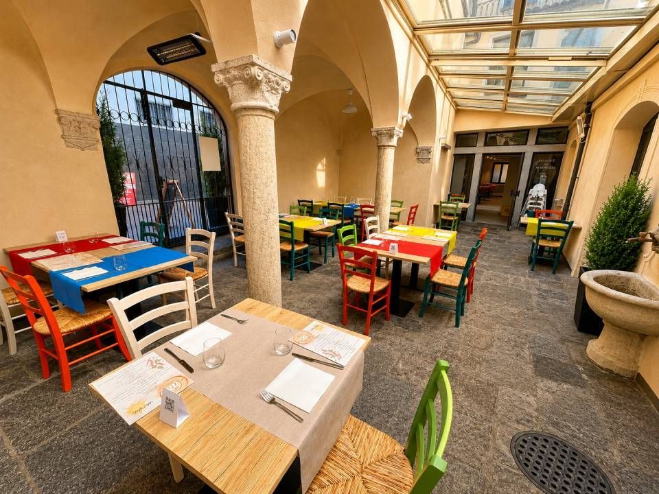 Cortile di un caffè all'aperto con tavoli e sedie colorati sotto colonnati ad arco in pietra.