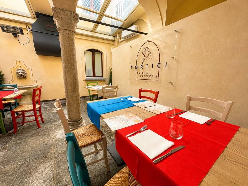 Terrazza esterna del caffè con tavoli, sedie e colonne in pietra rosse e blu, il tutto coperto da un lucernario.