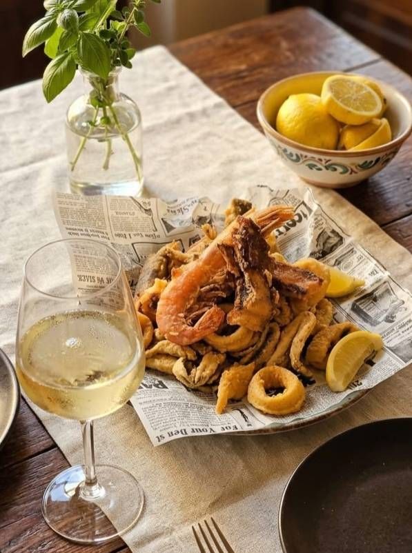 Un calice da vino e un piatto di frutti di mare fritti foderato di carta con spicchi di limone.