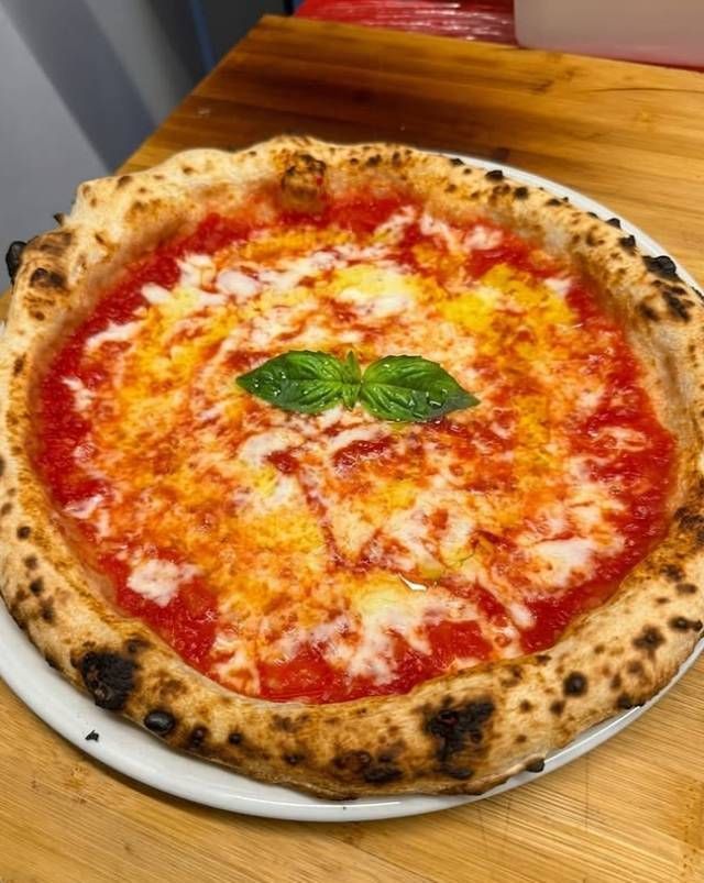 Pizza margherita cotta nel forno a legna su un piatto bianco con basilico, adagiata su un tavolo di legno.