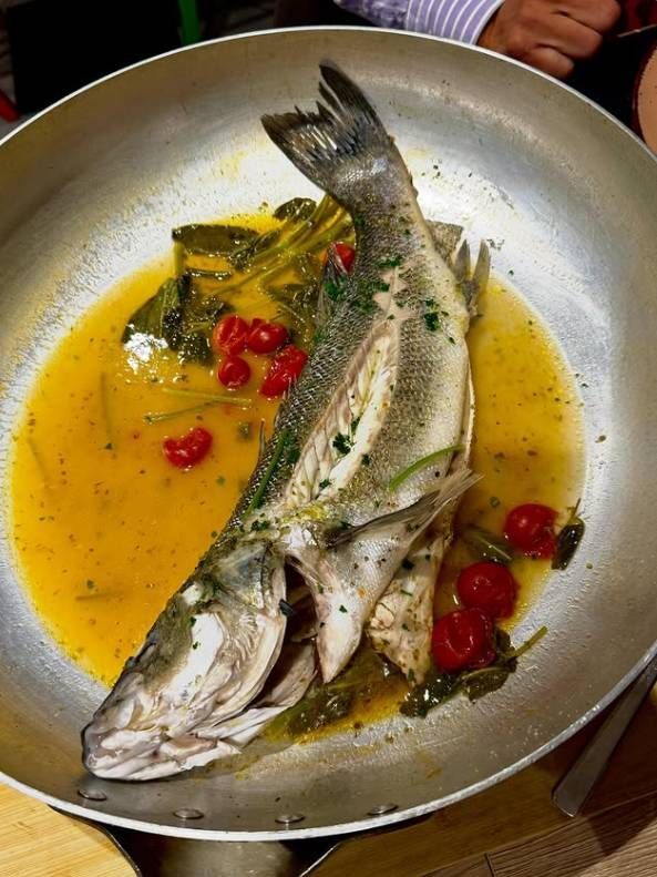 Pesce intero cotto a fuoco lento in salsa gialla con erbe aromatiche e peperoncini rossi in una padella di metallo