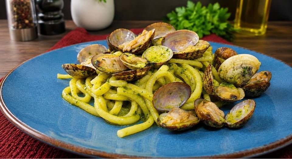 Piatto blu di pasta con funghi saltati ed erbe aromatiche su un tavolo di legno.