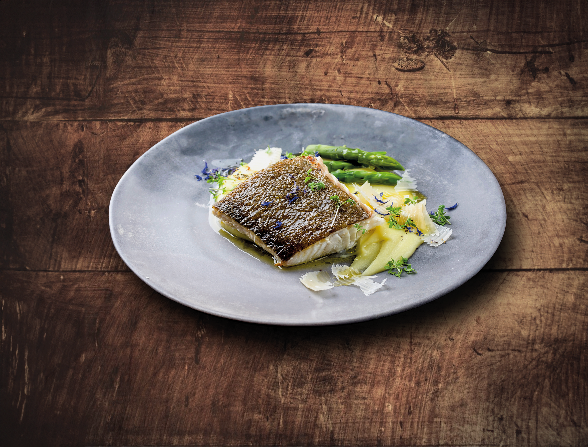 Assiette de poisson, purée de pommes de terre et asperges sur une table en bois rustique.