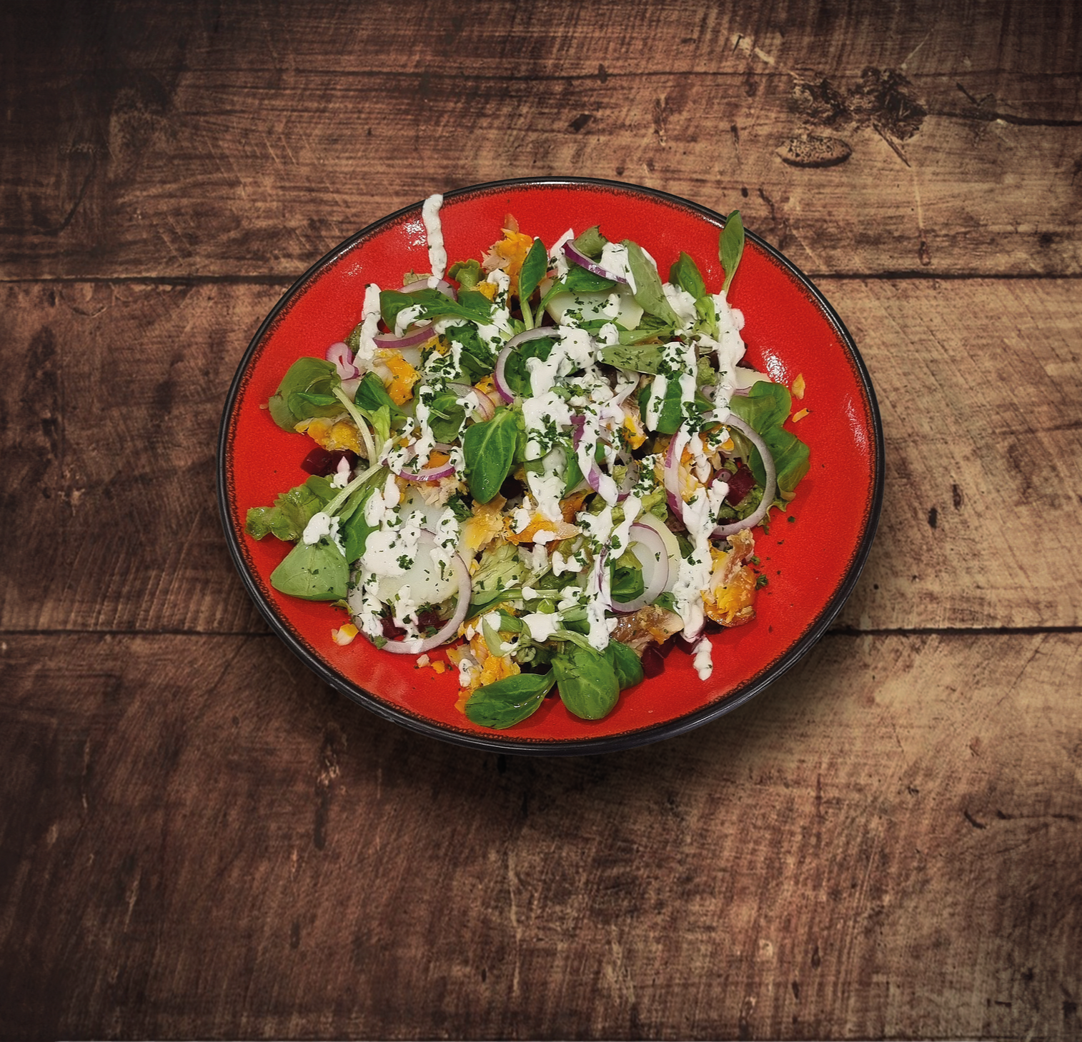 Salade avec légumes verts, oignons et vinaigrette sur une assiette rouge, posée sur une table en bois.