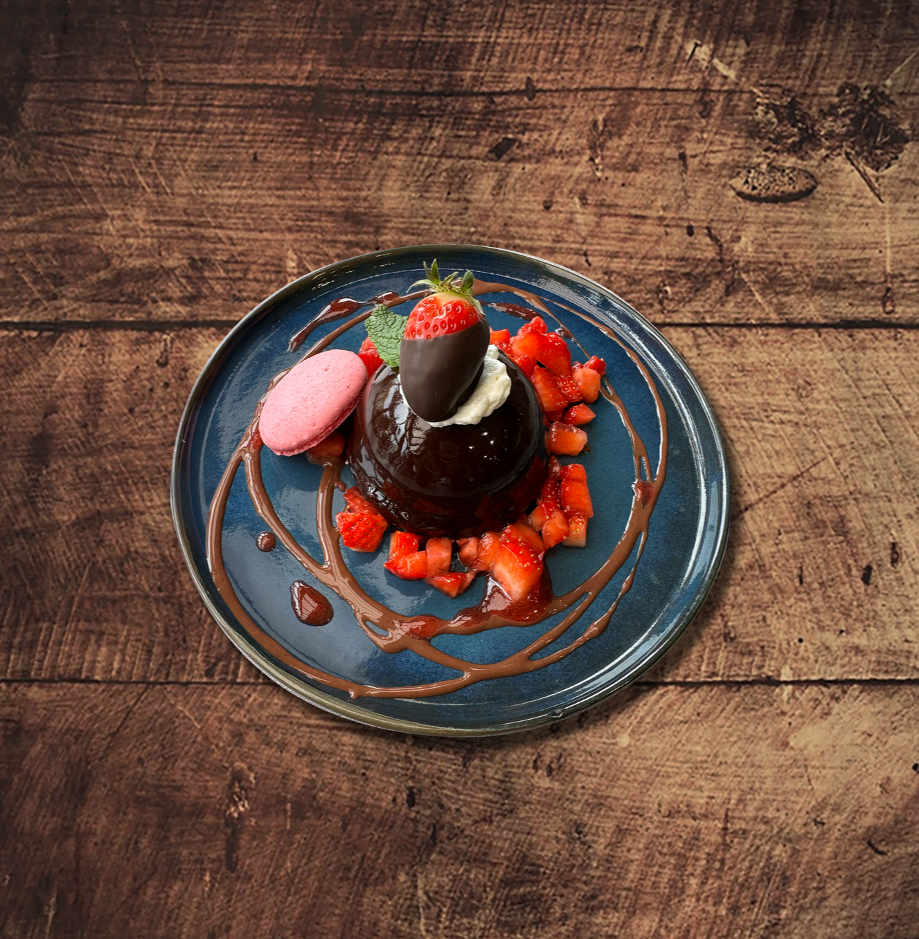Gâteau fondant au chocolat avec fraises enrobées de chocolat, fraises et macaron sur une assiette bleue.