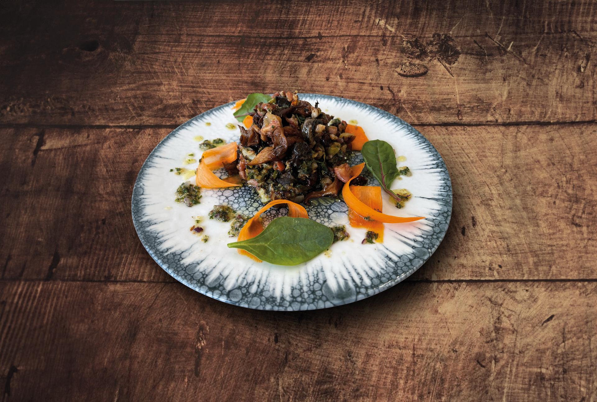 Assiette : céréales noires avec tranches d'orange, sauce verte et feuilles. Sur une table en bois.