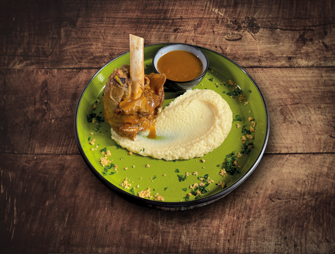 Jarret d'agneau braisé sur une assiette verte avec polenta et sauce