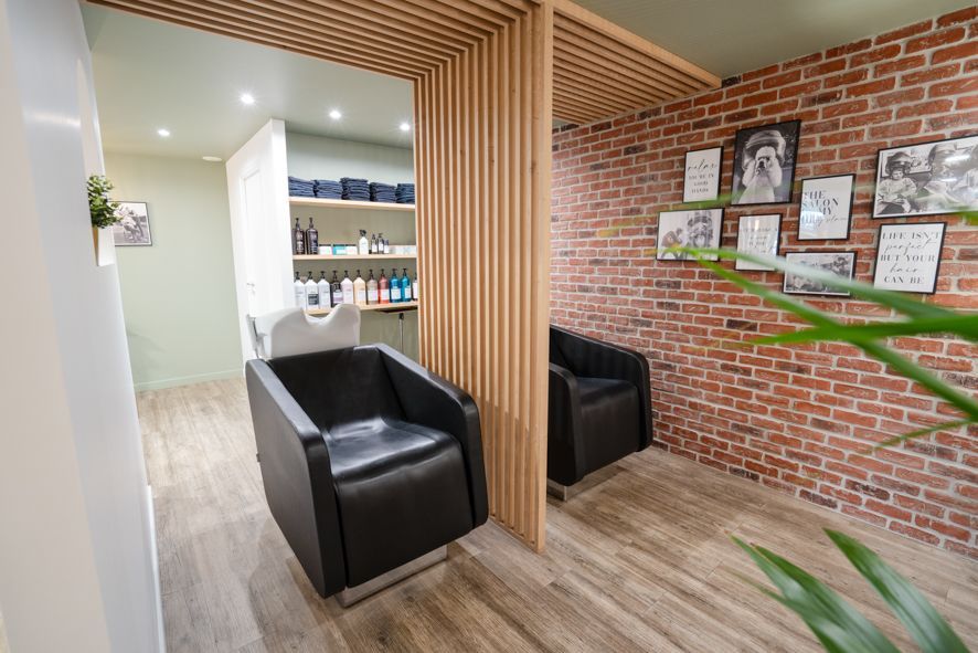 Salle d'attente moderne d'un salon de coiffure avec chaises noires, lattes de bois, mur de briques et décoration encadrée