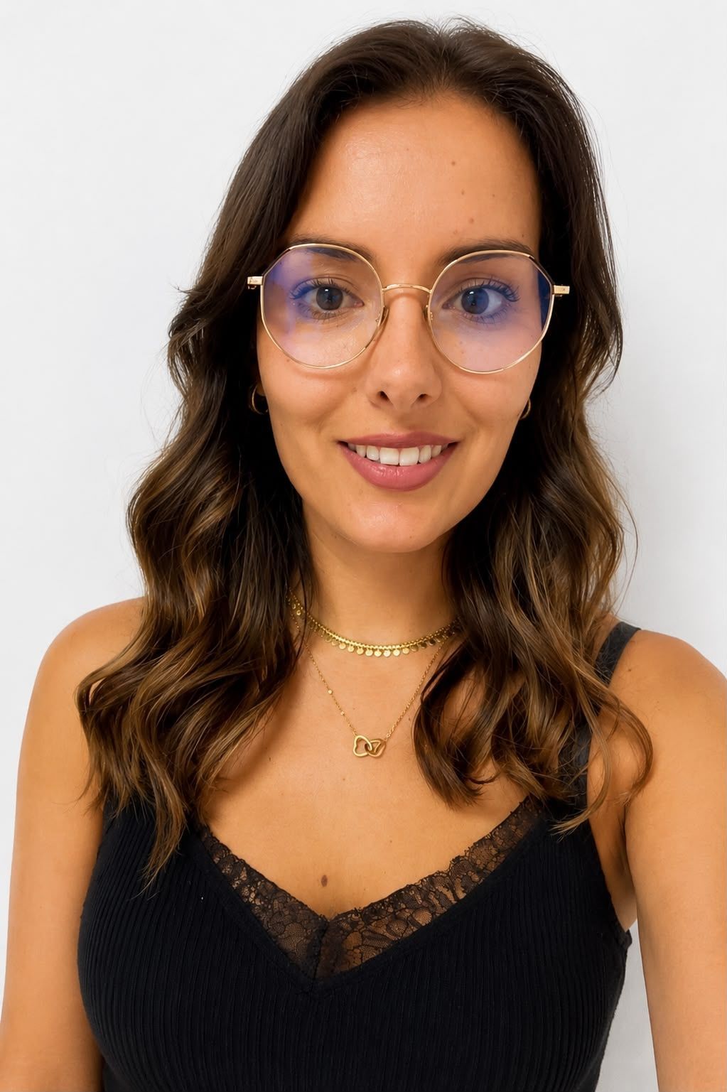 Femme souriante portant des lunettes et des cheveux bruns ondulés, vêtue d'un haut noir sur fond blanc