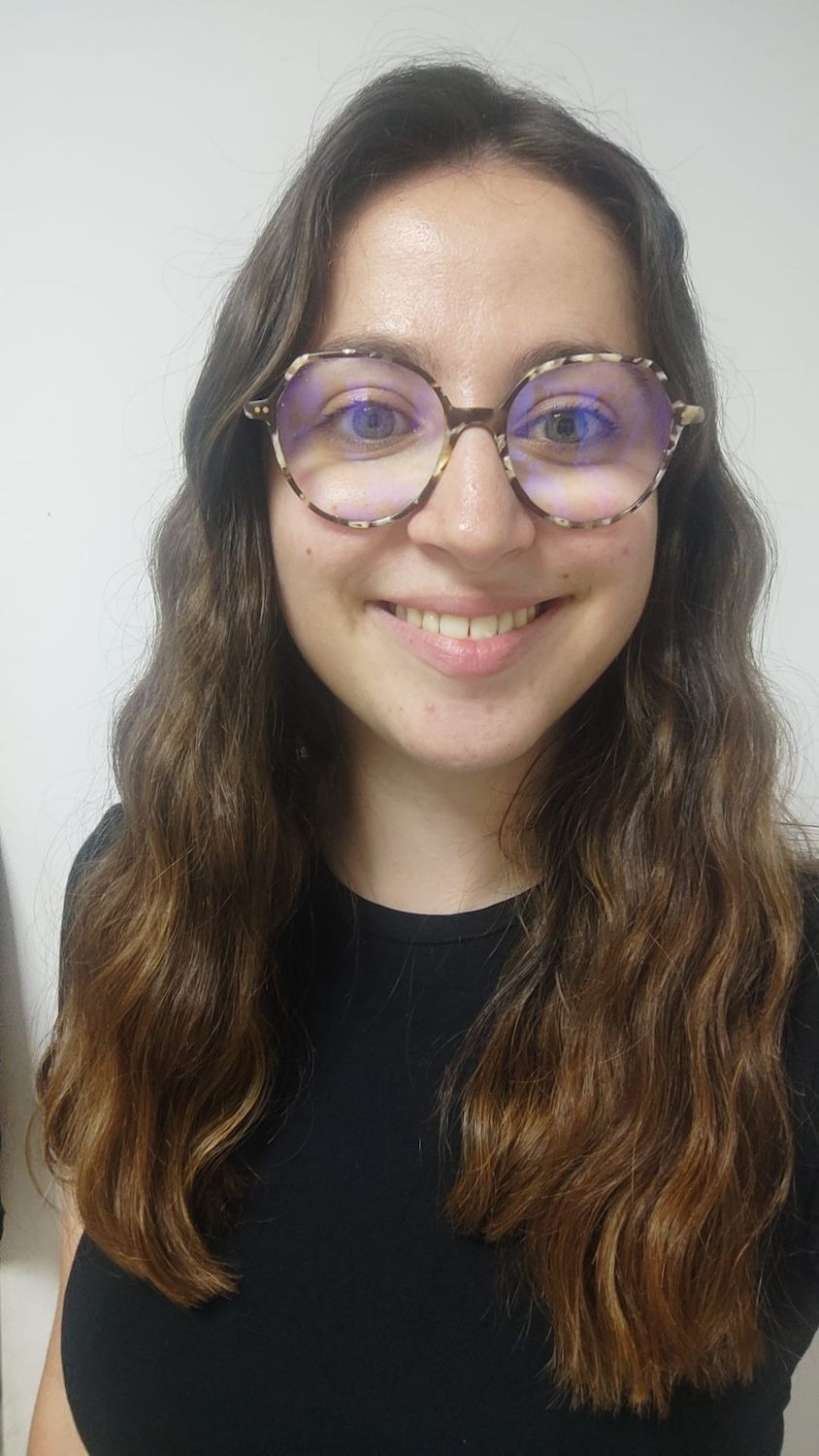 Personne souriante aux longs cheveux ondulés et portant des lunettes rondes, vêtue d'un haut noir sur fond clair