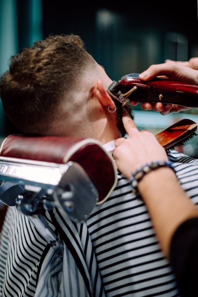 Un coiffeur coupe les cheveux d'un client avec une tondeuse sur un fauteuil de salon