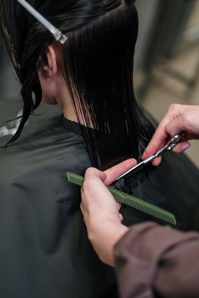 Coiffeuse coupant des cheveux foncés mouillés avec des ciseaux et un peigne au lavabo d'un salon.