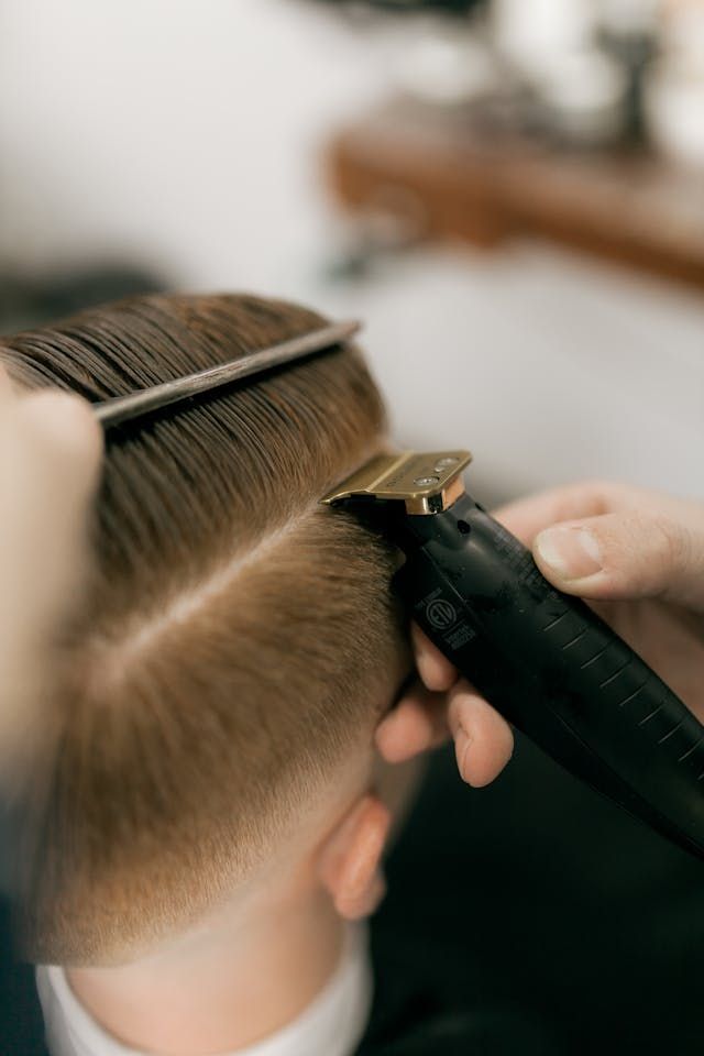 Un coiffeur réalise une coupe dégradée avec une tondeuse et un peigne.