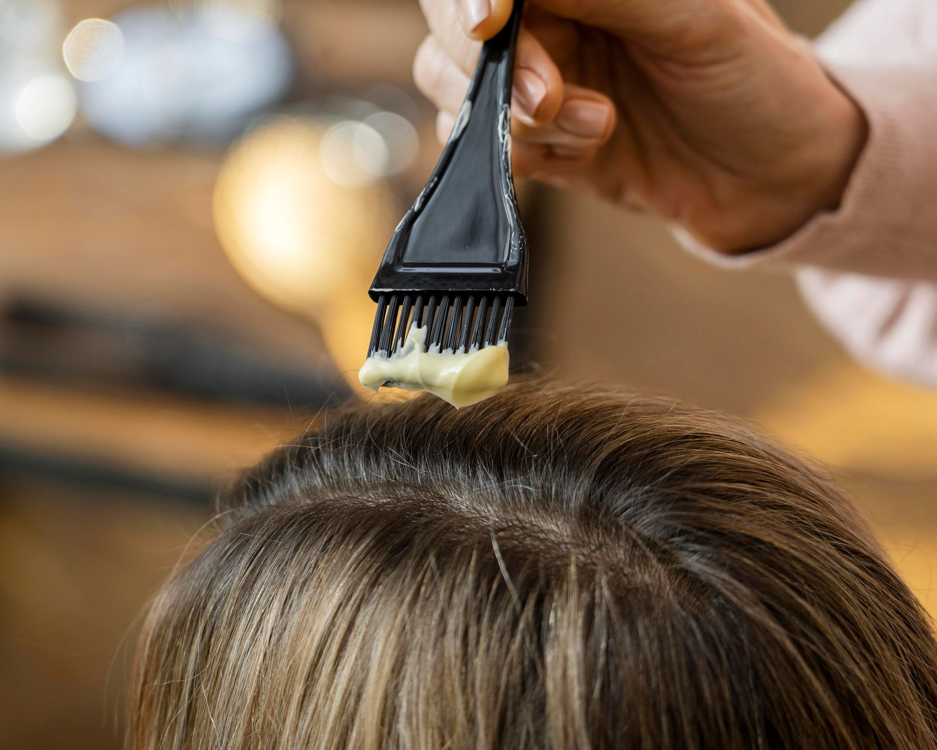 Application manuelle de teinture capillaire au pinceau sur les cheveux bruns d'une cliente dans un salon