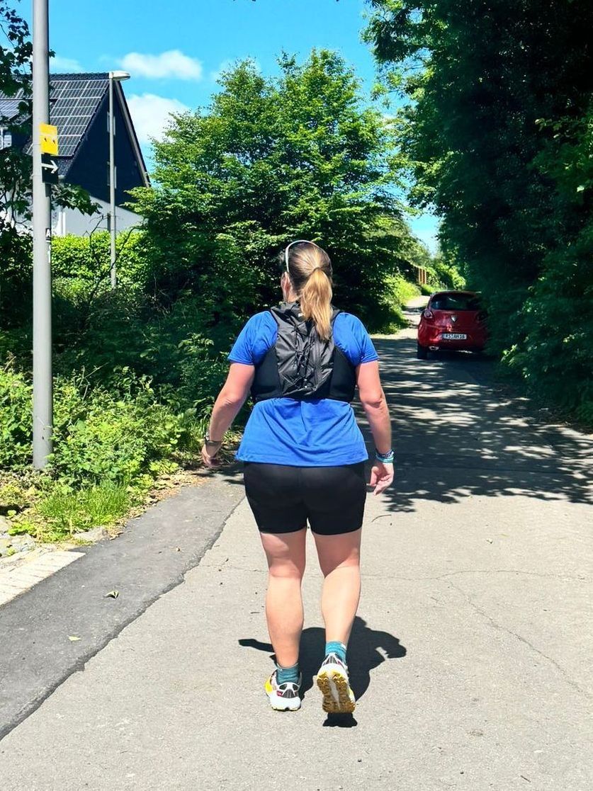 Eine Frau in einem blauen Hemd und schwarzen Shorts geht eine Straße entlang.