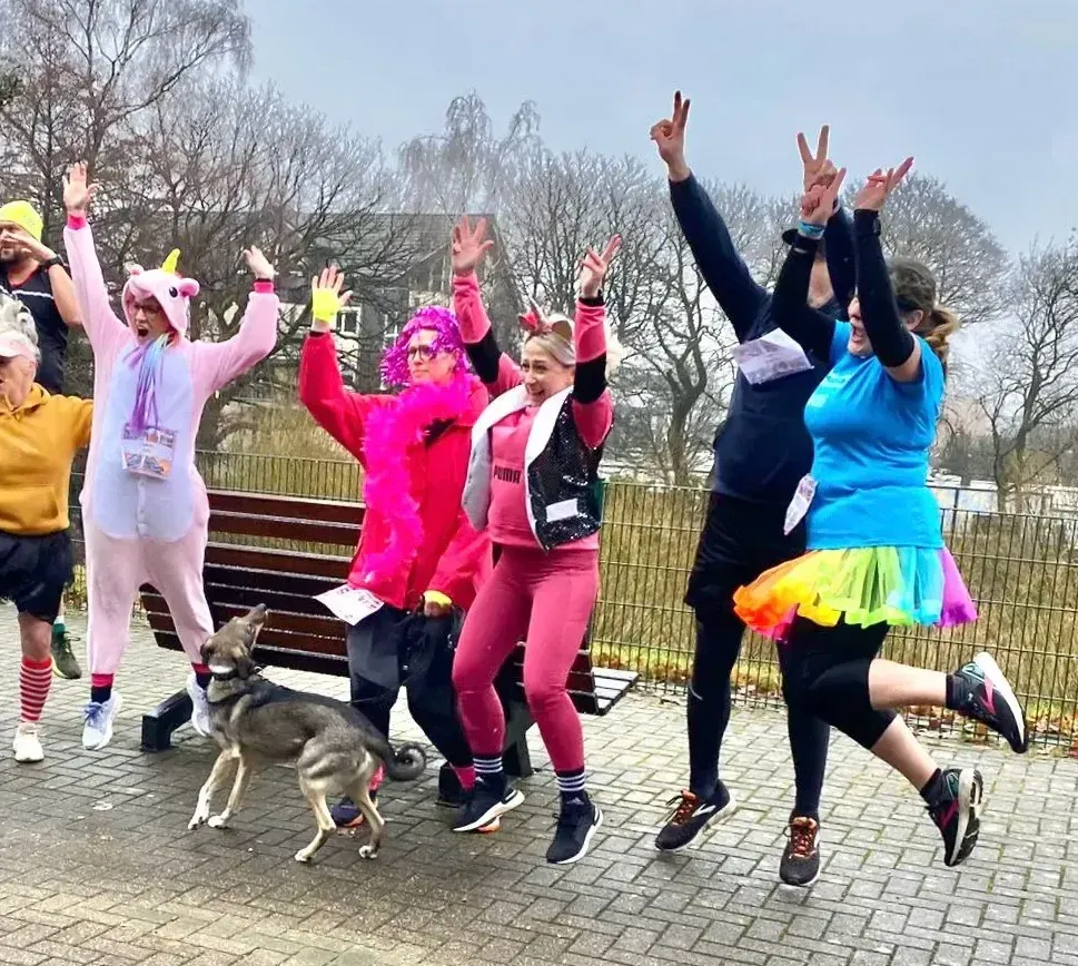 Eine Gruppe von Menschen in farbenfrohen Kostümen springt und feiert im Freien mit einem Hund.