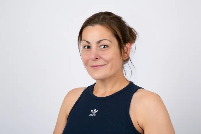 Frau in marineblauem Tanktop lächelt, Haare hochgesteckt, vor weißem Hintergrund.