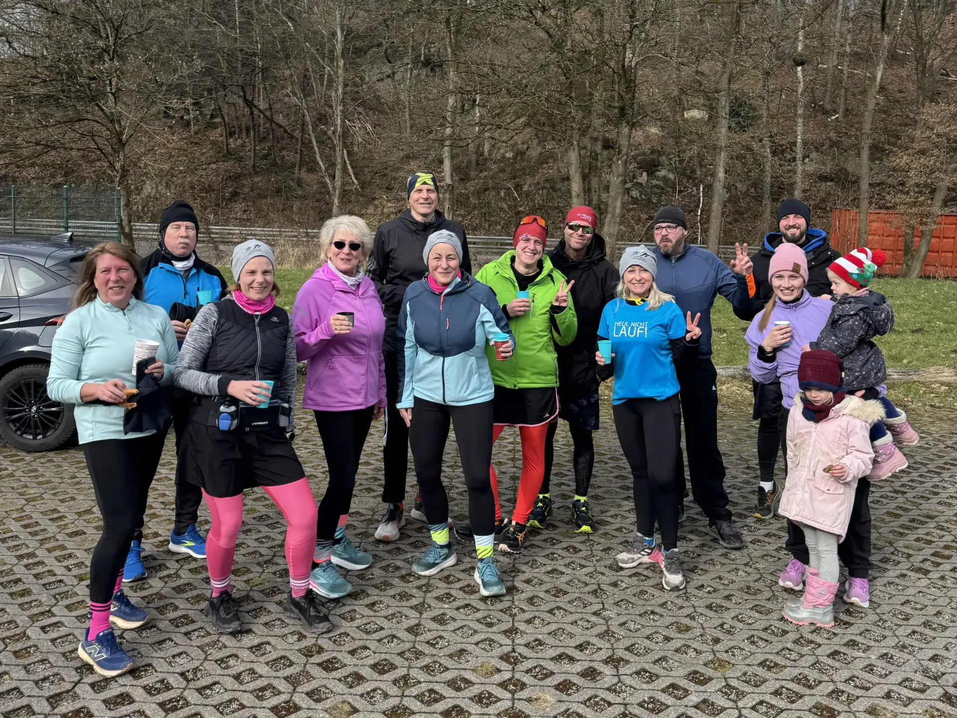 Eine Gruppe Läufer posiert im Freien, einige halten Becher in der Hand. Kühle, bewölkte Tage.