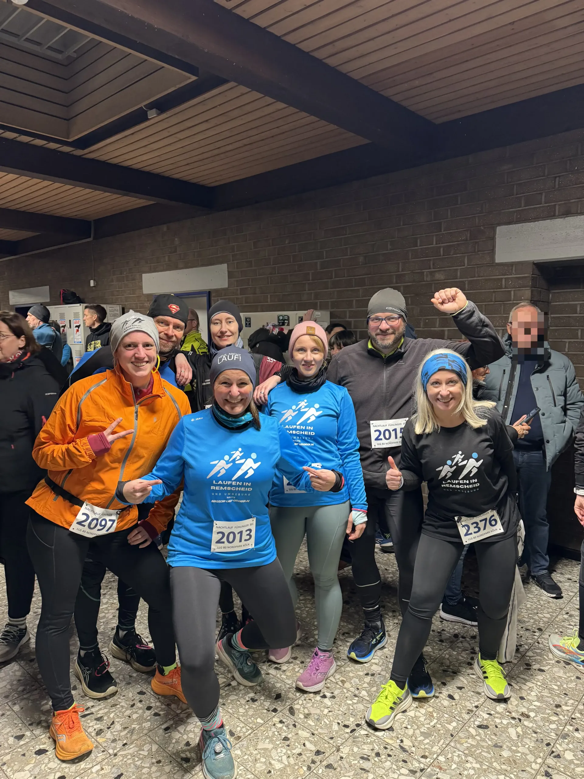 Eine Gruppe von Läufern posiert, lächelt und lässt bei einer Veranstaltung ihre Muskeln spielen; Innenraum mit Backsteinmauer.