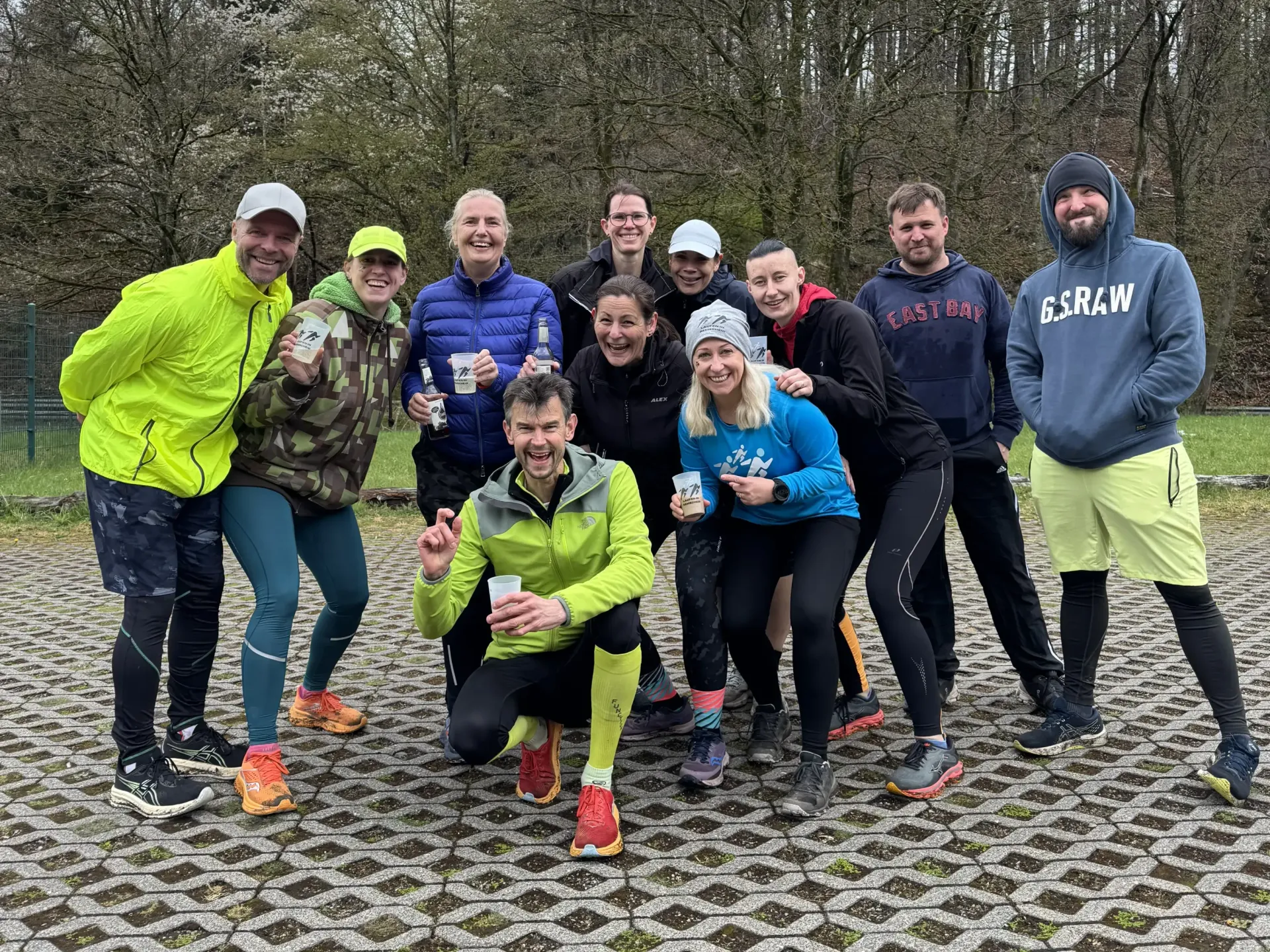 Eine Gruppe lächelnder Menschen posiert nach einem Lauf an einem bewölkten Tag im Freien in Sportkleidung.