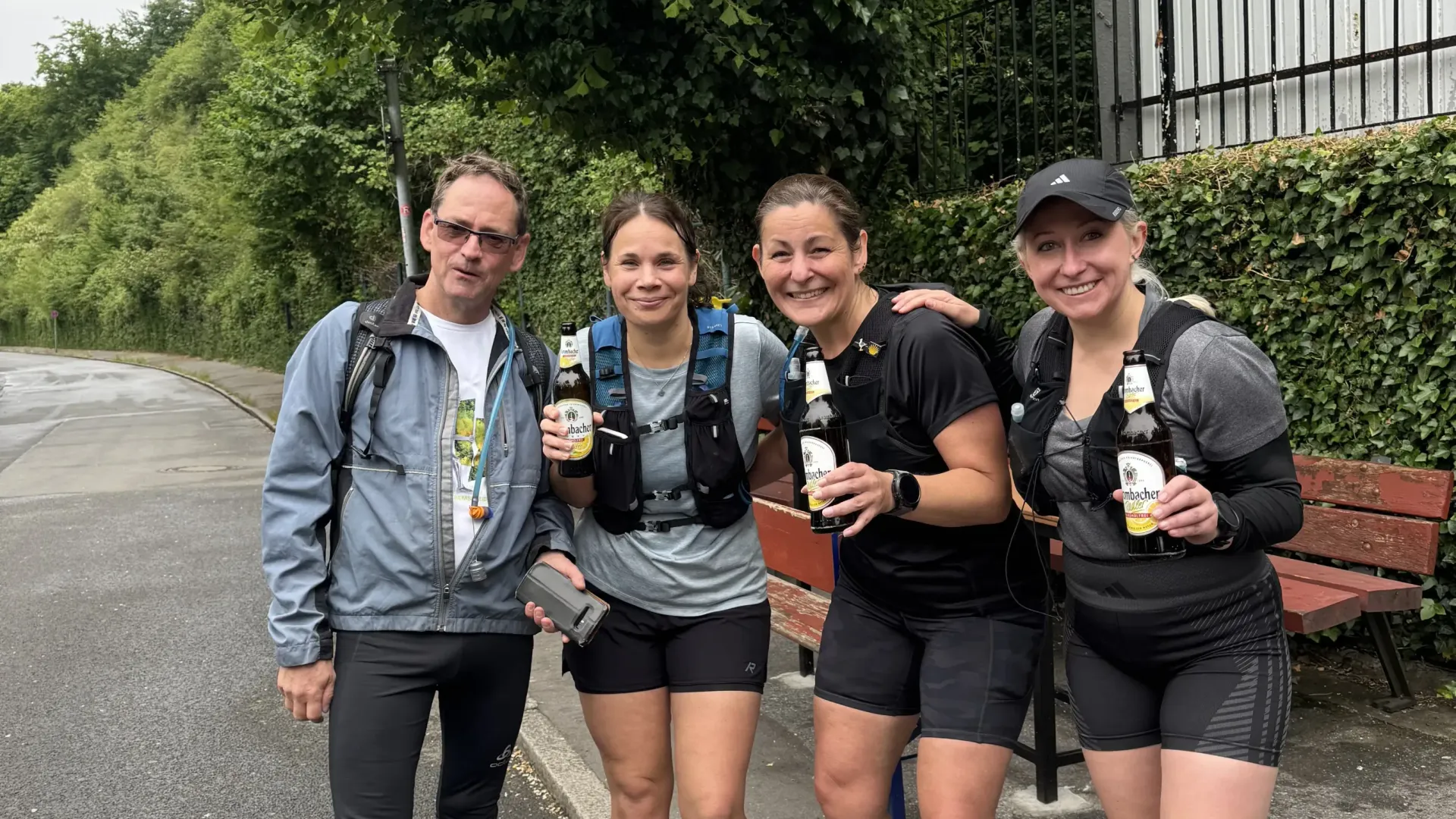 A group of people standing on a sidewalk holding bottles of beer.