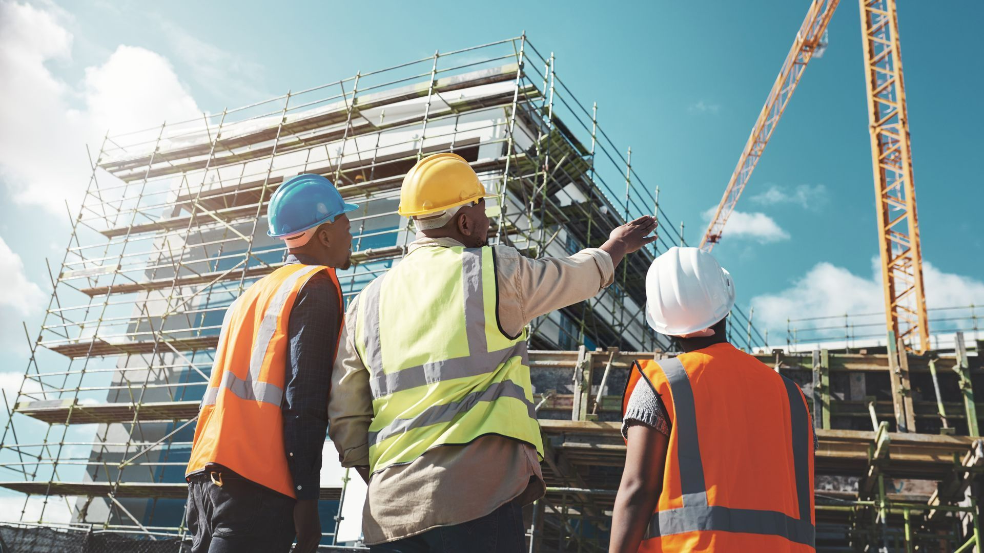 3 personnes casquées et de dos pointant vers un bâtiment en construction