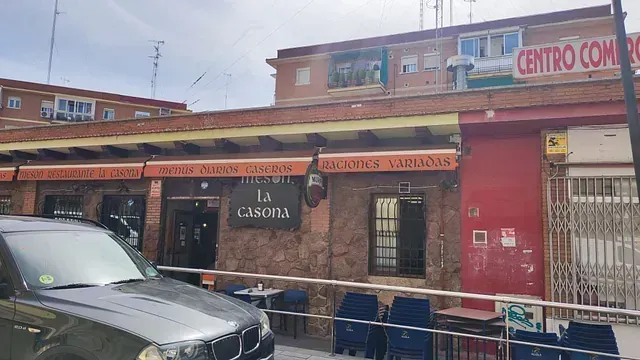 Un coche está aparcado delante de un edificio con mesas y sillas.