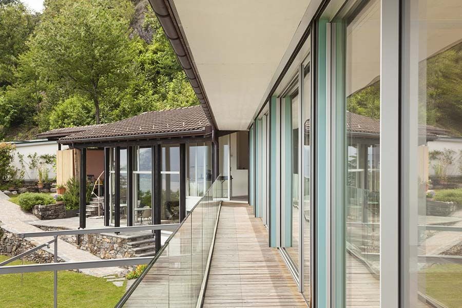 Un pasillo largo en una casa con barandilla de vidrio y muchas ventanas.