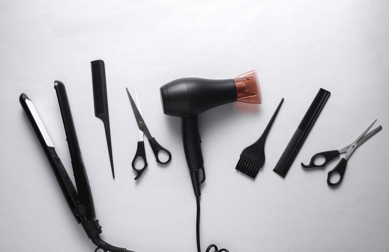 Outils de coiffure disposés sur un fond blanc, notamment un sèche-cheveux, des peignes, des brosses et des ciseaux