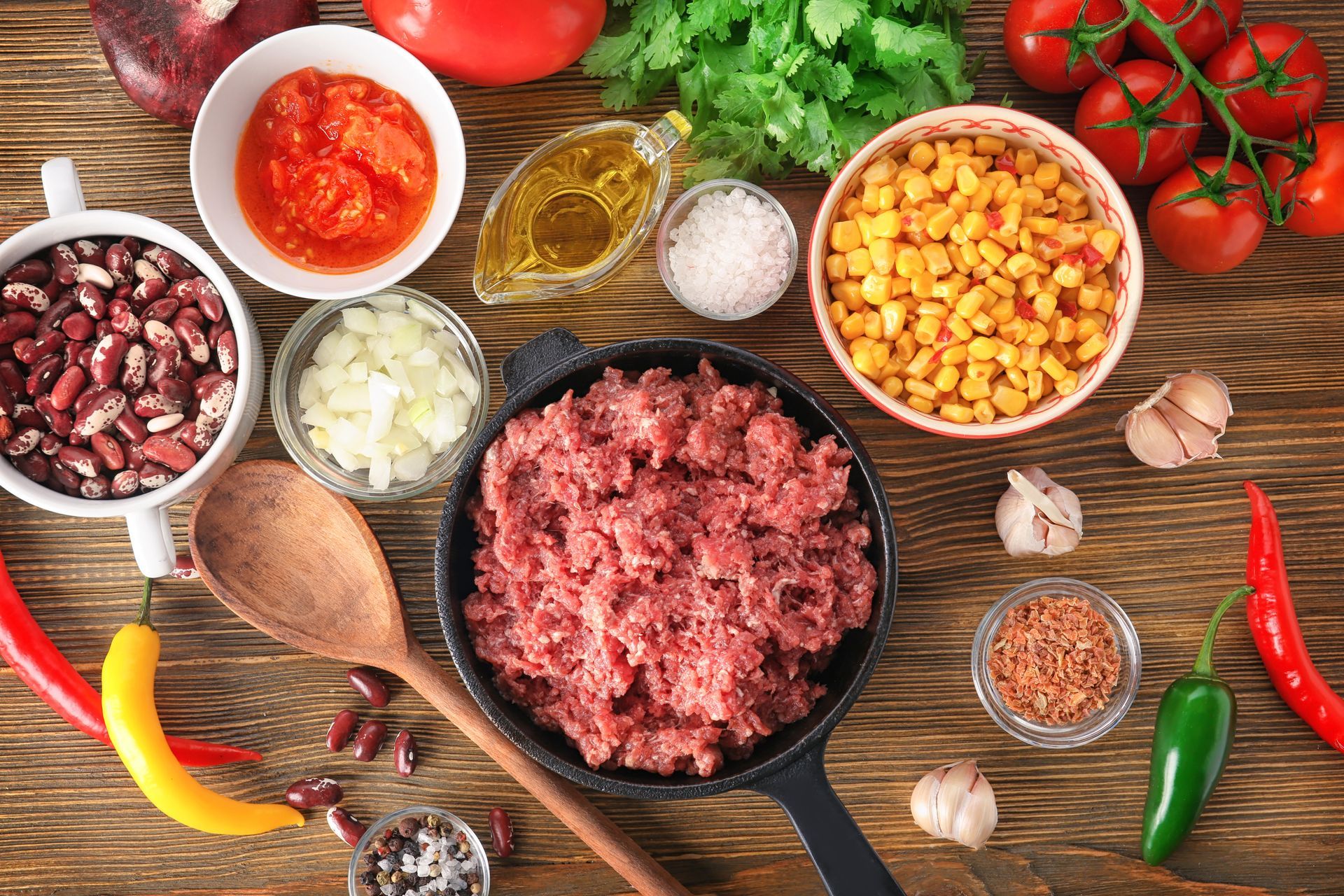 Viande hachée et ingrédients divers disposés sur une table en bois pour préparer une sauce spaghetti