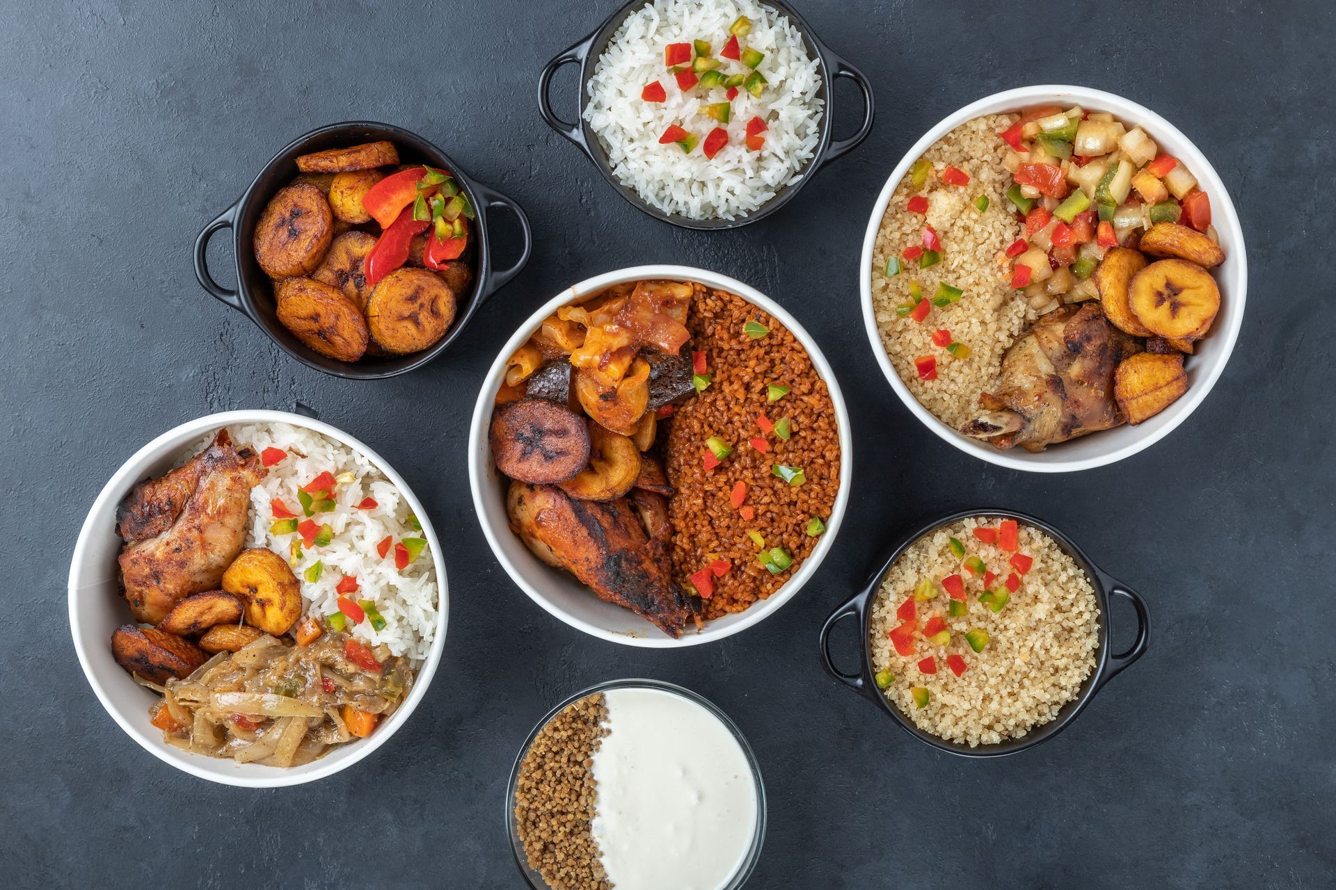 Divers plats colorés servis dans des bols sur une table sombre, notamment du riz, du curry et des aliments frits.
