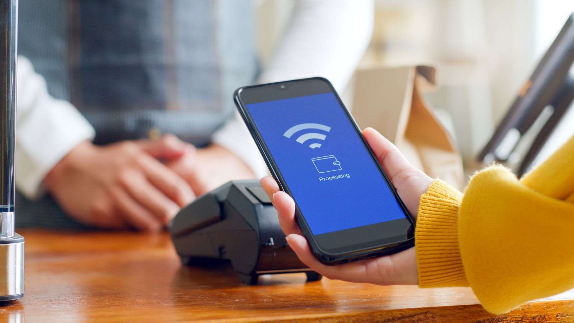 Une personne utilisant un smartphone pour effectuer un paiement sans contact sur un terminal de paiement, à la table d’un café