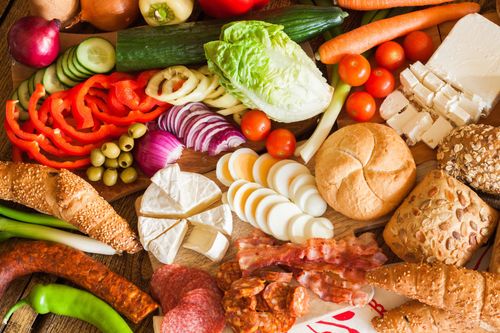 Divers fruits et légumes frais, pain, fromage et viande disposés sur une surface en bois