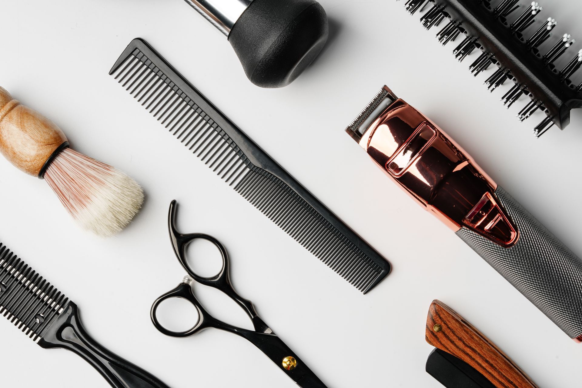Divers outils de coiffure — peignes, ciseaux, brosse et tondeuse — disposés sur un fond blanc