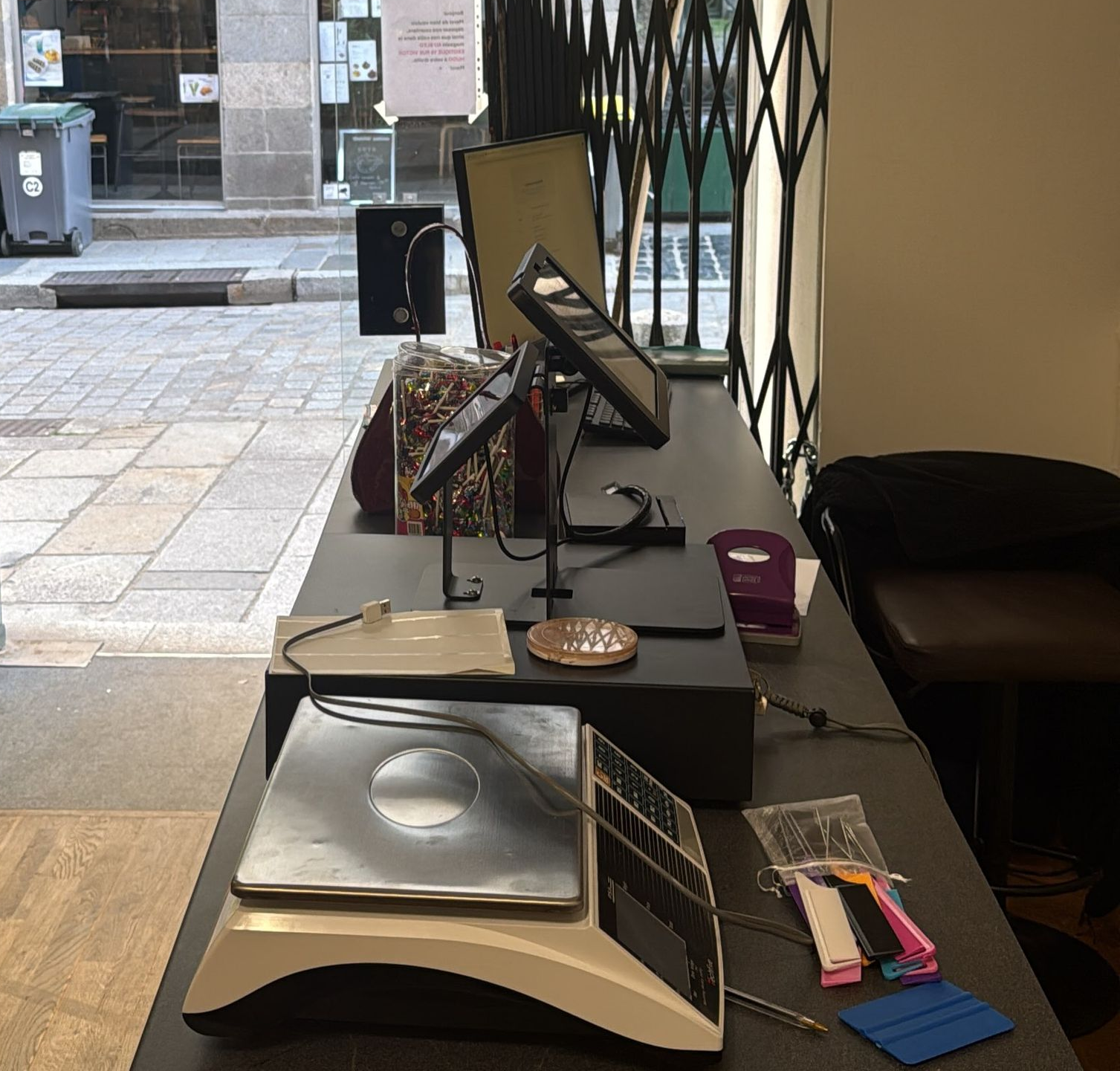 Intérieur de boutique avec une porte ouverte donnant sur une rue pavée de pierres et des vitrines à l’extérieur.