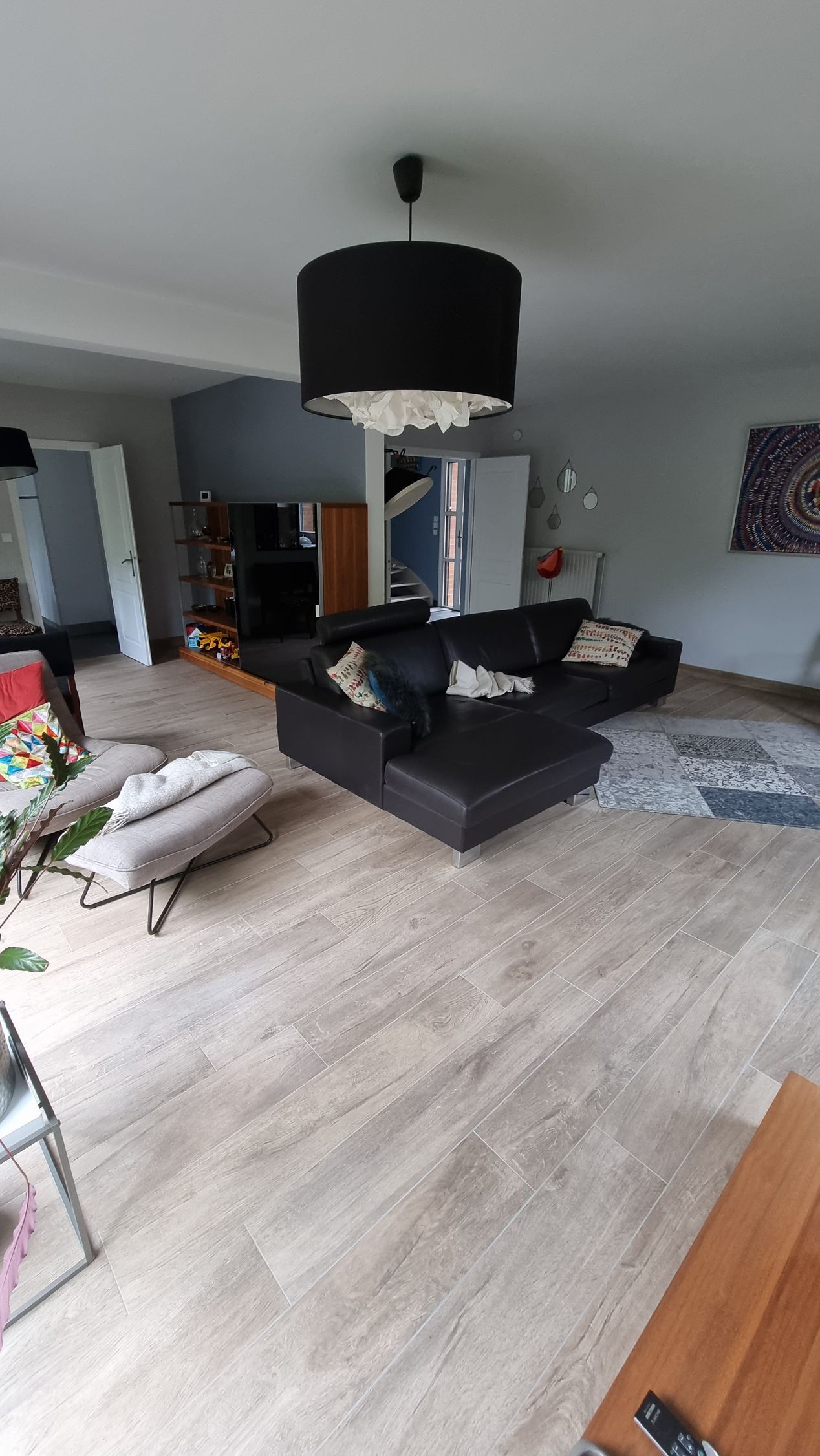 Salon moderne avec canapé d'angle noir, murs gris, lampe suspendue et parquet clair