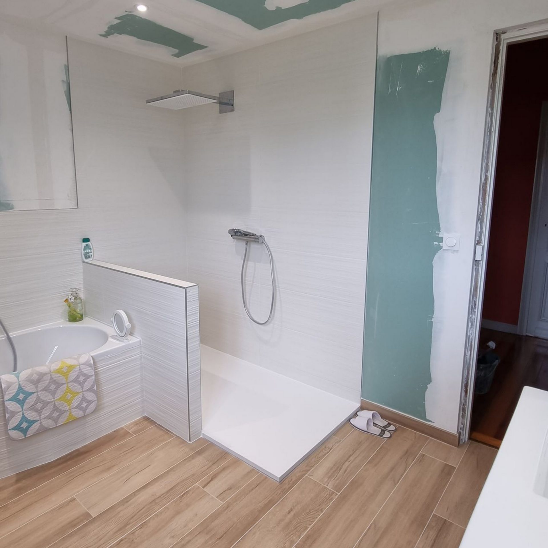 Salle de bains en rénovation avec douche carrelée, cloisons sèches apparentes et sol imitation bois.