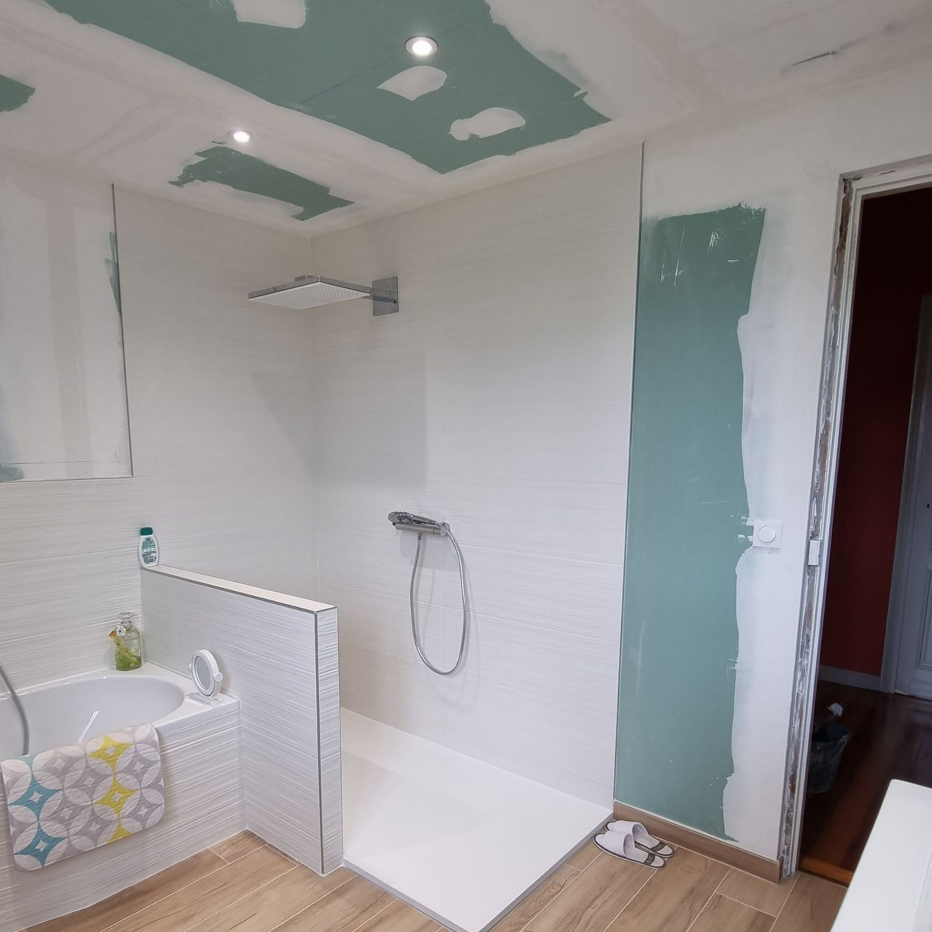 Salle de bains partiellement rénovée avec murs carrelés blancs, taches vertes au plafond et baignoire à gauche