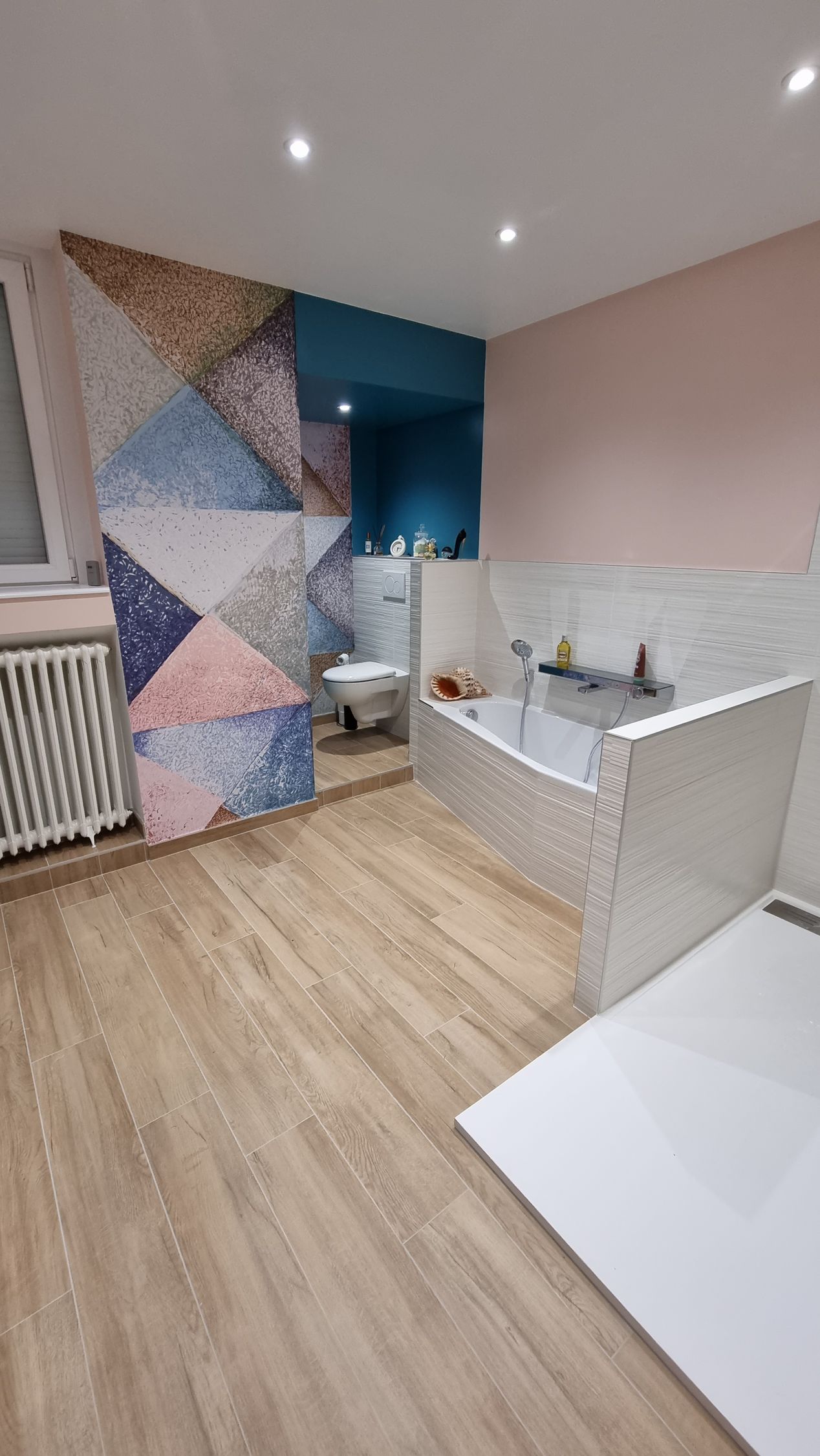 Salle de bains moderne avec mur d'accent géométrique, lavabo blanc, sol imitation bois et éclairage encastré au plafond