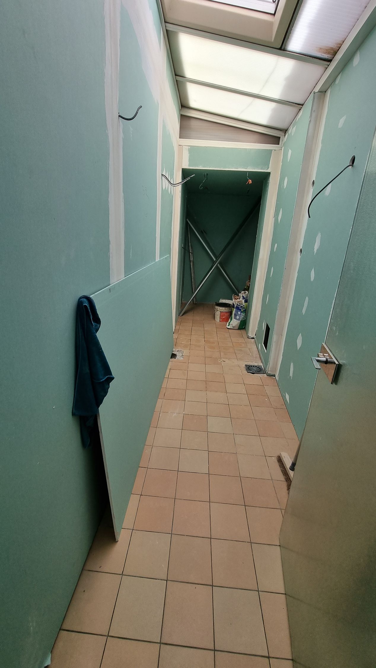 Couloir étroit carrelé aux murs vert pâle, avec une serviette accrochée à gauche.