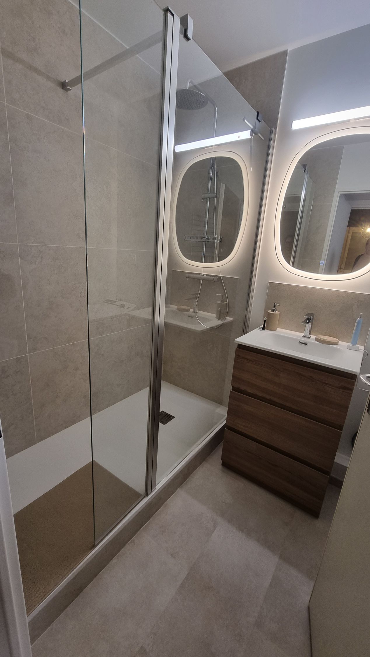 Salle de bains moderne avec cabine de douche en verre, double miroir éclairé et meuble-lavabo en bois.