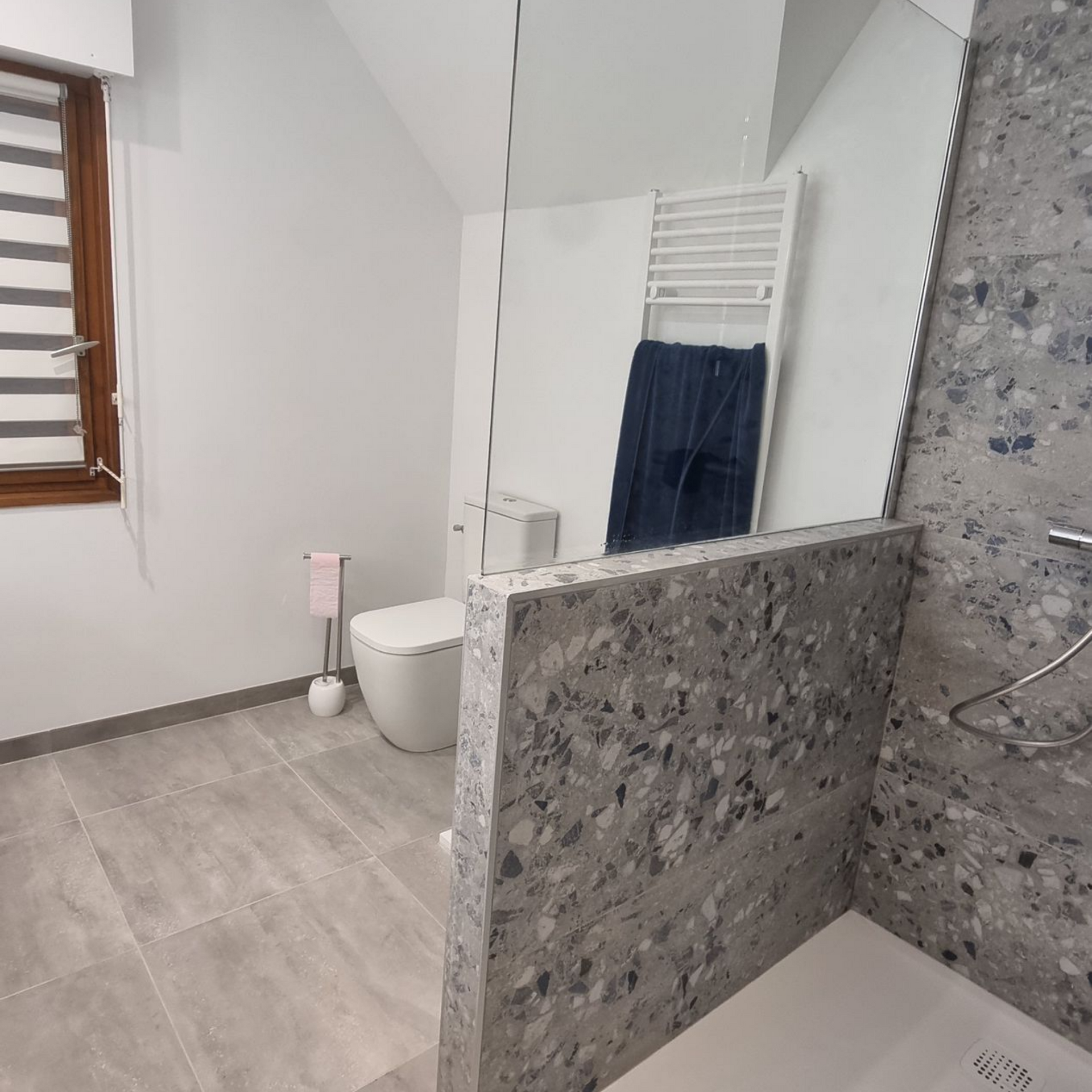 Salle de bains moderne avec toilettes, douche, cloison en pierre grise, fenêtre et porte-serviettes