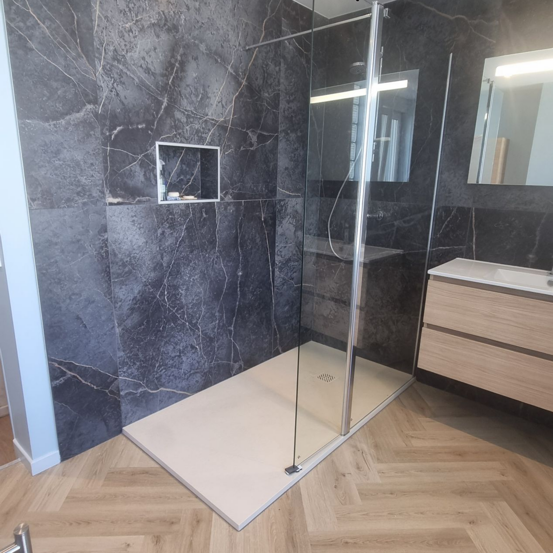 Salle de bains moderne avec paroi de douche en marbre noir, paroi de douche en verre, receveur de douche blanc et meuble-lavabo en bois.